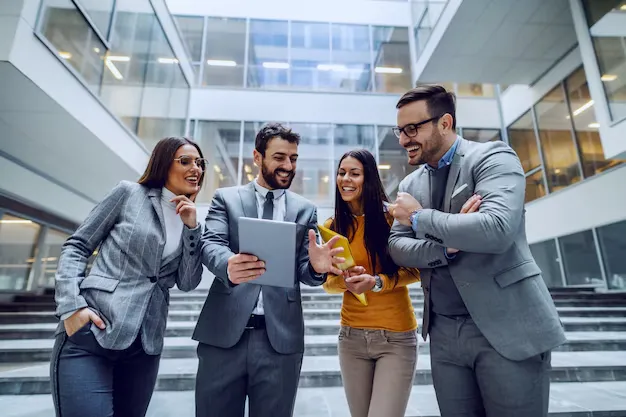 Four Successful Smiling Businesspeople Standing Front Corporate Building Looking Tablet That Man Middle Holding